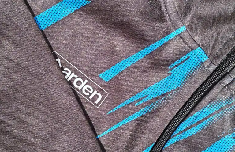 Gros plan sur la maille technique d'un vêtement de sport foncé, montrant des motifs dynamiques cyan et le logo Arden près d'une couture