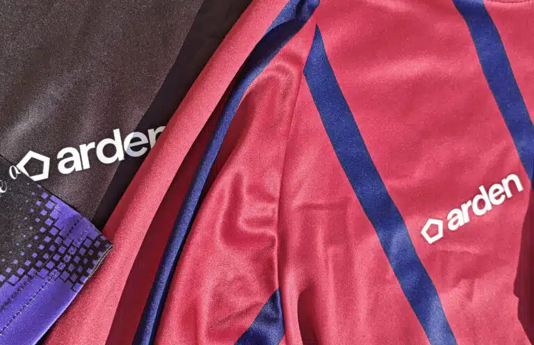 Plan rapproché sur deux tissus de maillots de sport, l'un sombre avec des motifs géométriques violets, l'autre rouge à rayures diagonales bleues, tous deux avec le logo Arden